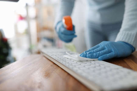Female hands in rubber gloves wiping keyboard with antiseptic napkin in office. Disinfection of computer equipment during covid-19 pandemic conceptの写真素材