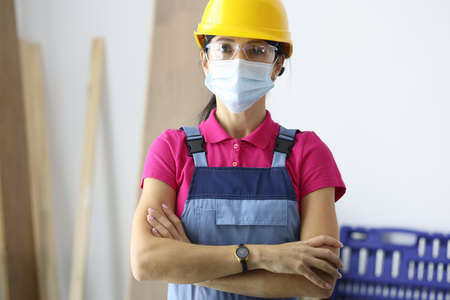 Woman in protective helmet wearing medical mask on face standing at construction site.Repair services during covid-19 pandemic conceptの写真素材