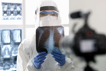 Doctor in protective suit shows an X-ray to camera. Lung screening in coronavirus pandemic concept