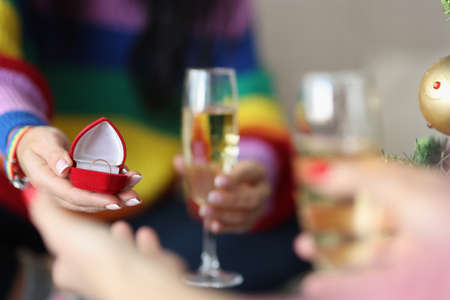 Womans hand holds box with a wedding ring and a glass of champagne. Hand and heart proposals in gay...