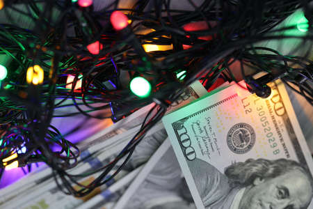 Dollar bills lying on table near sparkling garland for new year. Christmas costs conceptの写真素材