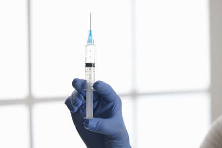 Doctors hand in rubber glove holding syringe with medicine in clinic closeup. Vaccine prophylaxis...