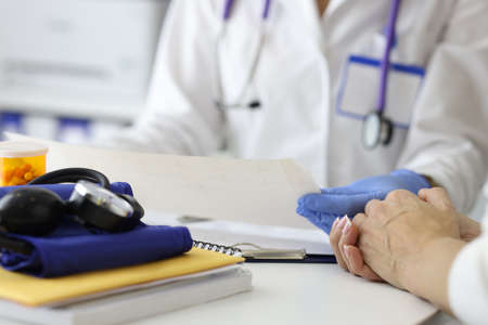 Doctor holding cardiogram in gloves in hands and advising patient in clinic closeup. ECG diagnostics of rhythm disturbances conceptの写真素材