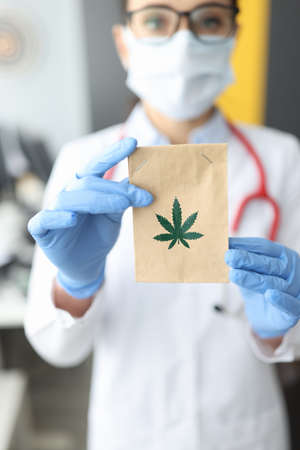 Doctor in rubber gloves holding paper bag with marijuana in clinic closeup. Treatment of cancer with narcotic drugs conceptの写真素材