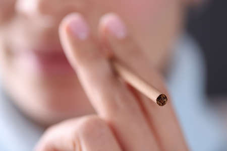 Woman holding cigarette in hand near her mouth closeup. Harm of smoking concept