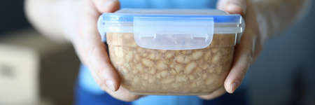 Male loader shows plastic box with homemade food. Worker in uniform shows food in container. Vegan nutrition for life and health. Variety menu improves quality life. Separation energy consumption bodyの写真素材