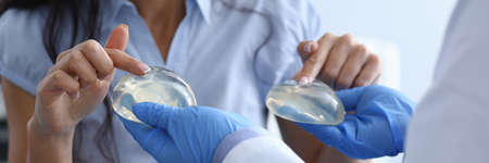 Laughing woman chooses breast implants from doctor. Doctor offers girl choice silicone breast implants. Medical consultation or recommendation plastic surgeon. Enlarge the breast and change its shapeの写真素材