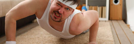 Kind brunette man making face while doing push-ups activity, looking straight at camera during trainingの写真素材