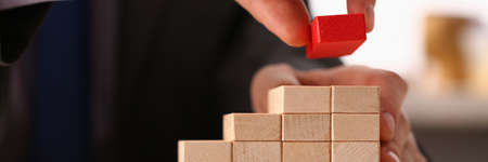 Kind businessman using wooden blocks for making visual scheme of his development at work