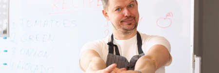Pleased brunette male person keeping smile on his face while wearing apron and looking at camera