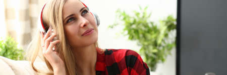 Beautiful young woman keeping smile on her face while sitting on cozy sofa at homeの写真素材