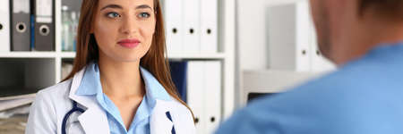 Attentive doctor being in all ears while listening to her visitor, wearing sterile medical uniformの写真素材