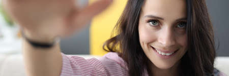 Brunette woman smiles and greets with her hand. Positive online communication concept