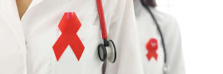 Doctors stand with phonendoscope around their neck and red ribbon on uniforms close-up. World aids...