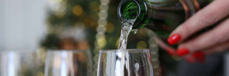 Female hand pours champagne into glasses against background of New Years decorations. New Years...