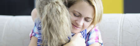 Little girl with mom hugging on couch at home. Trust relationship between parent and child concept