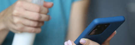 In hand smartphone is being sprayed with an antiseptic. Dangerous bacteria on mobile phone concept