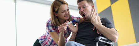 Surprised man in wheelchair and joyful woman are looking at pregnancy test. Replenishment in...