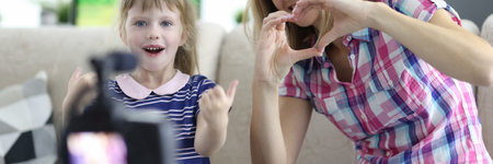 Woman with child is sitting on couch in apartment and showing hand gesture in front of camera. Family business blogging concept.の写真素材
