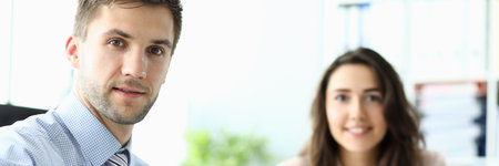 Handsome male worker handing paper and looking at camera while charming lady holding clipboard and smilingの写真素材