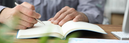 Close up of young man sitting at the table and making notes at workの写真素材