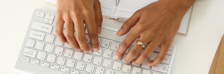 Close up of young woman working on modern computer while sitting at the table with notebook