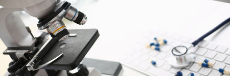 Close up of white table with laboratory optical microscope, pharmaceutical drugs, keyboard and medical device for listening to internal sounds of bodyの写真素材