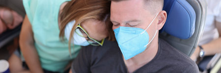 Man and woman in medical protective masks are sleeping in aircraft cabin. Safe travel for health in coronavirus pandemic conceptの写真素材
