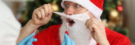 Doctor in protective suit taking smear pcr from santa claus near Christmas tree. Examination of animators before contact with children conceptの写真素材