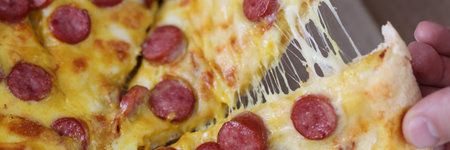 Male hands tearing off slice of pizza with cheese and sausage close-up. Fast food delivery conceptの写真素材