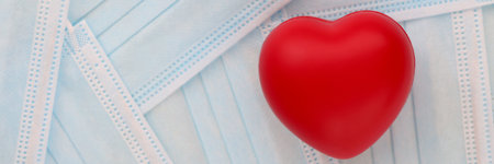 Red toy heart lying on table among medical protective masks in clinic. Complication of...