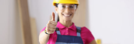 Smiling woman in construction overalls showing her thumb closeup. High-quality construction works conceptの写真素材