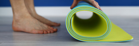 Close-up of person closing down mat for yoga. Finished workout. Comfy material for exercise. Adult bare feet on laminate floor. Sport and active lifestyle conceptの写真素材