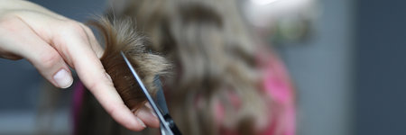 Close-up of mother holding metal scissors and cutting strand of luxury childs hair. Home hairdresser and creating haircut indoors. Salon in room. Kid and parent spare time togetherの写真素材