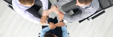 Top view of businesspeople putting hands together in office. Good deal. Support and team work. Employees sitting on chairs in stylish suits. Business and career success conceptの写真素材