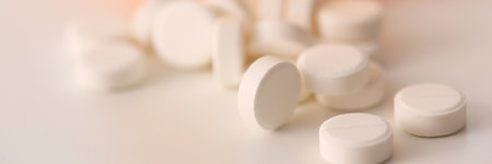 Close up of round medicine poured out of orange pack on plane surface isolated on white backgroundの写真素材