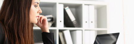 Young woman sitting at desk with pen and cup of hot drink while using notebookの写真素材