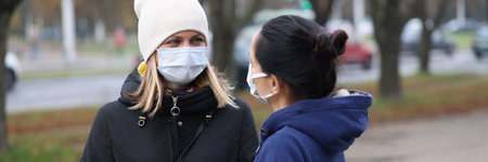 Two young women communicating in protective face masks outside. Safety rules during the covid-19...