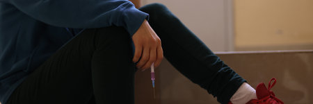 Addict sits with his head down and holds syringe in his hands. Depression and drug addiction conceptの写真素材