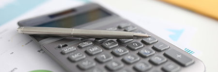Gray calculator lay on document with text and diagram close-up. Gray metal lay rest on computer hardware.の写真素材