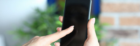 Female hands in the office holds a smartphone on a brick wall background. Black screen phone. Damage...