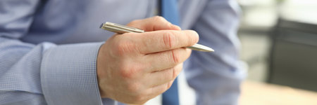 A man in business clothes holds a silver pen close up. Remote specialist consultation during a pandemicの写真素材