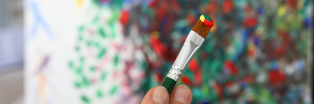 Hands of the artist hold a brush with paint. Female hands draw a large bright abstract drawing