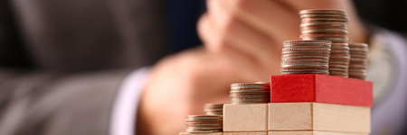 Close up of man sitting near wooden cube with golden coin on table. Trade profit and money concept