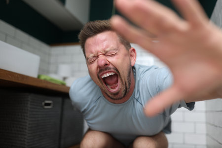 An emotional man sits in toilet and screams in pain. How to treat chronic constipation conceptの写真素材