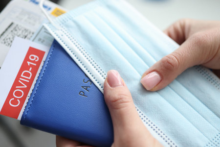Female hand holding covid-19 vaccination passport and plane tickets closeup. Traveling abroad during coronavirus pandemic conceptの写真素材