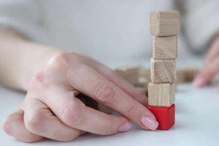 Female hand pulling out red wooden cube from base of tower closeup. Financial pyramid conceptの写真素材