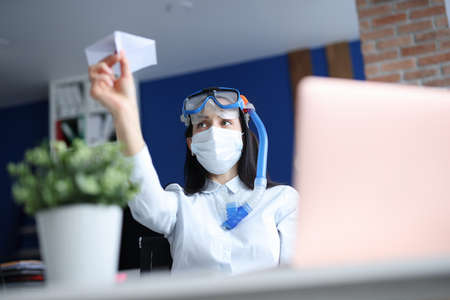 Woman in medical facemask and diving mask launching paper plane. Closed borders during pandemic conceptの写真素材