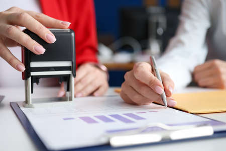Business women signing document and certifying seal closeup. Signing contracts concept