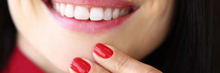 Close-up of young woman with perfect white smile. Female with fresh bright red manicure. Trendy...